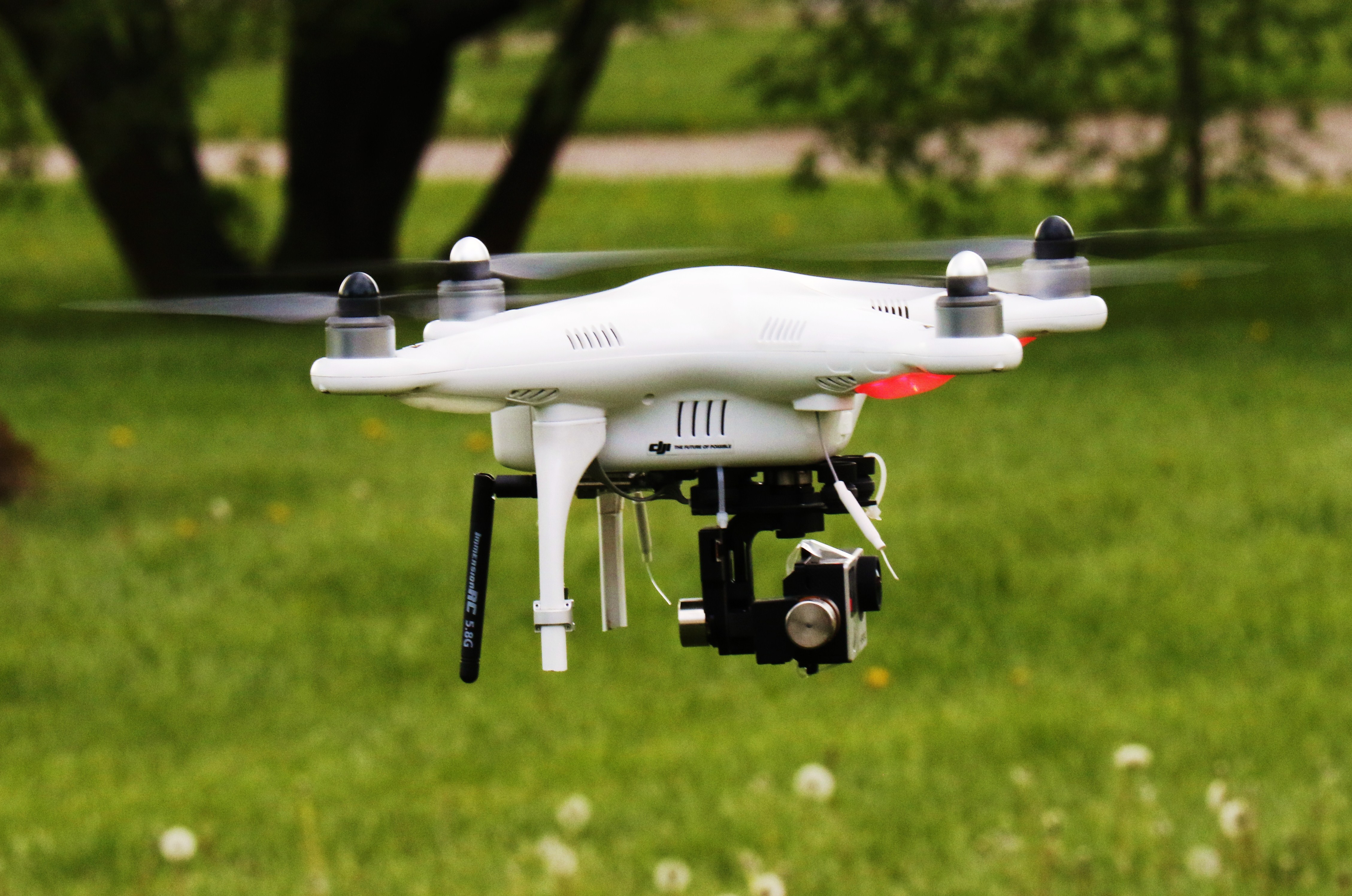 different white Drone flying over the grass with a camera mounted below it